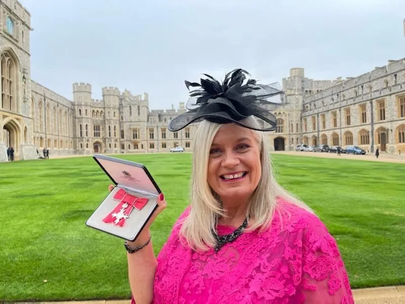 Alison holding her MBE medal in its case in the quadrangle at Windsor Castle.