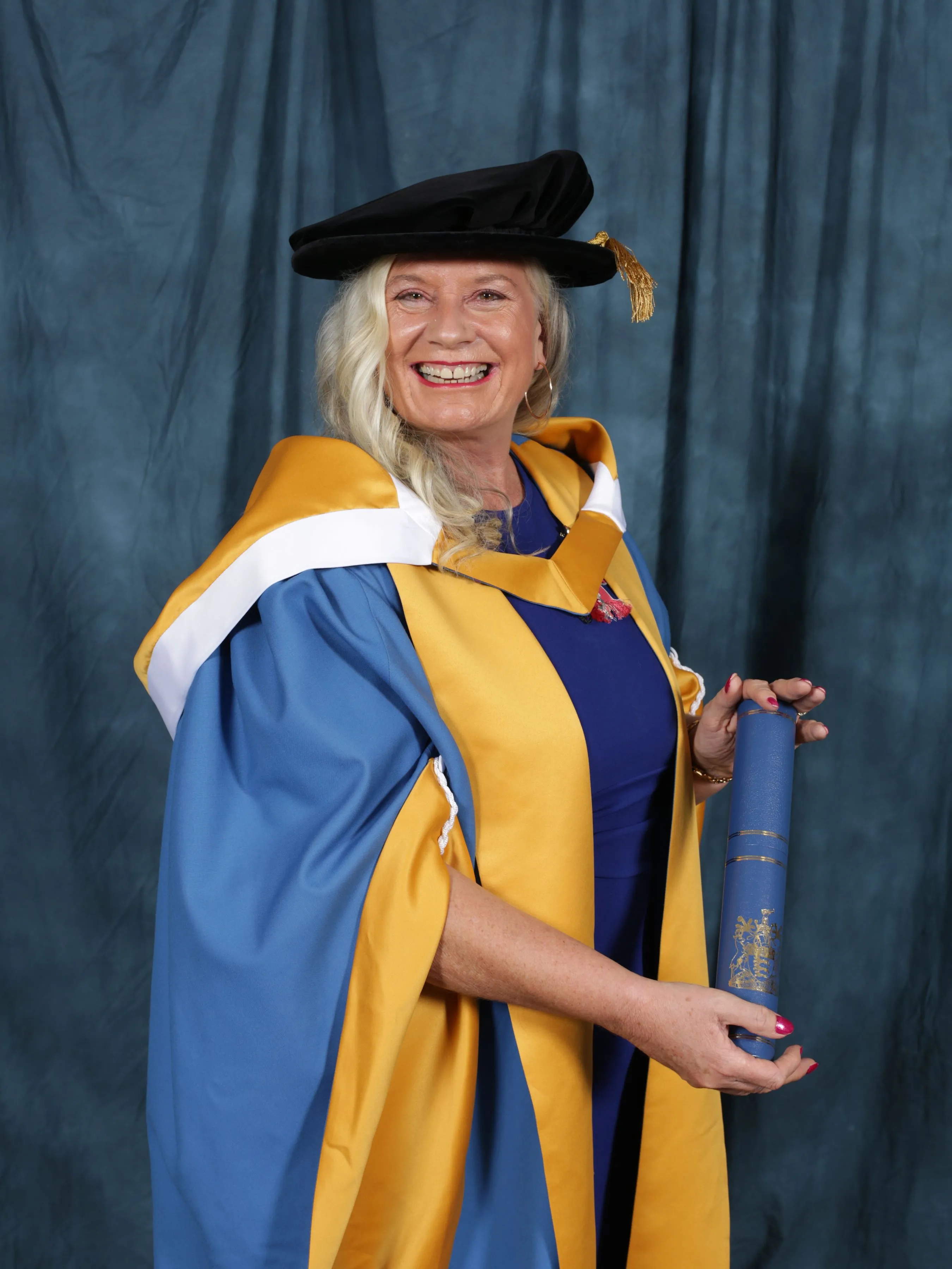 Dr Alison Edgar in doctoral robes, holding her honorary doctorate scroll.