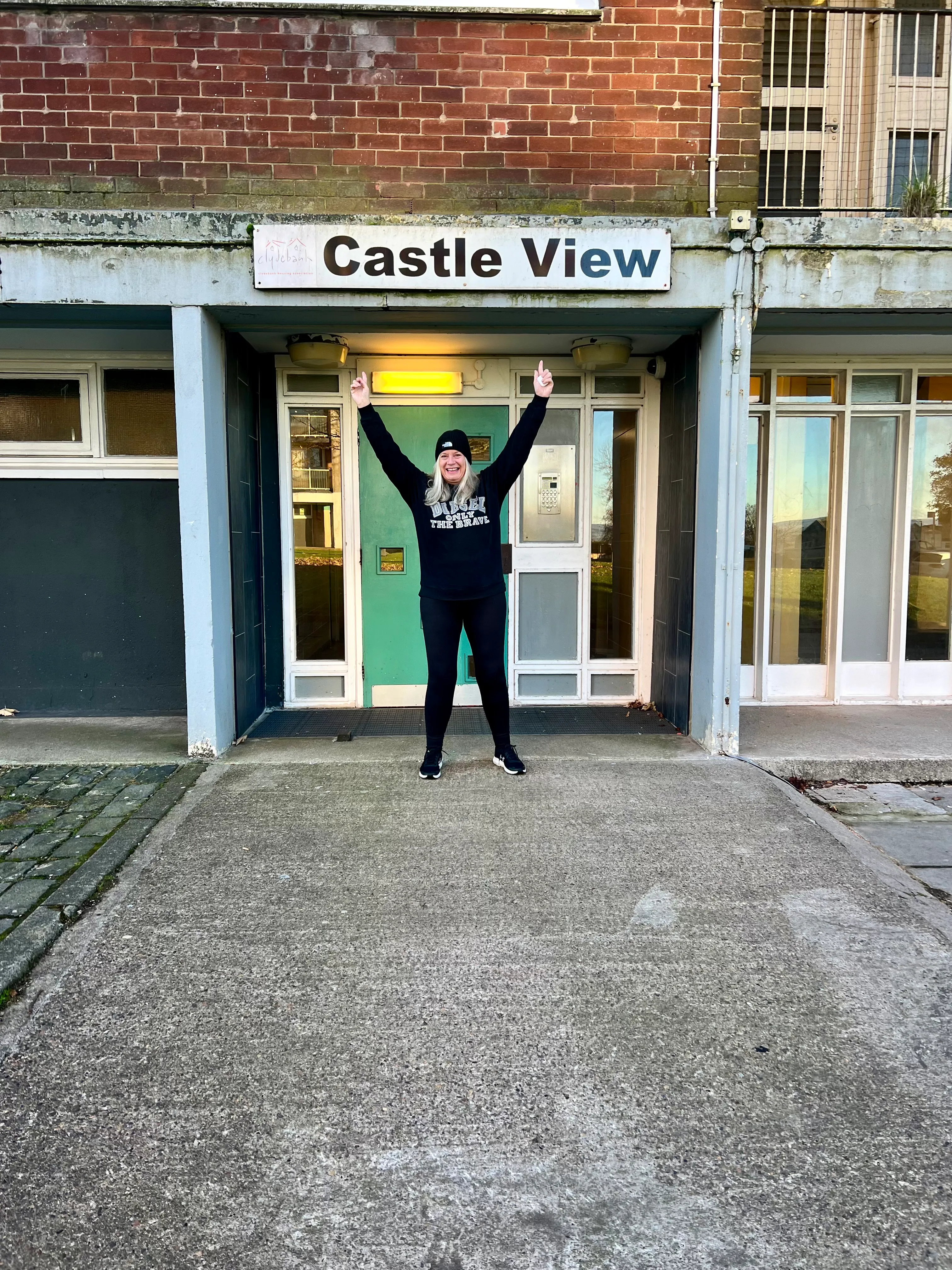 Dr Alison Edgar, arms raised, back at the Clydebank council flats where she grew up.